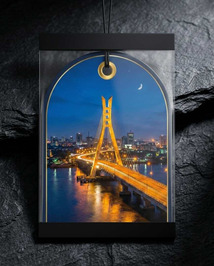 A rectangular black-framed wall art print or plaque featuring an arched nighttime city bridge scene with glowing yellow bridge lights over blue water, displayed against a dark textured stone background.