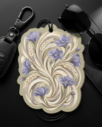 A decorative car air freshener tag with a vintage floral design, styled on a dark surface with sunglasses and a key fob.