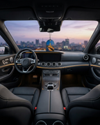 A luxury car interior with black leather seats, a dark dashboard, wood trim accents, and a city skyline visible through the windshield at dusk.