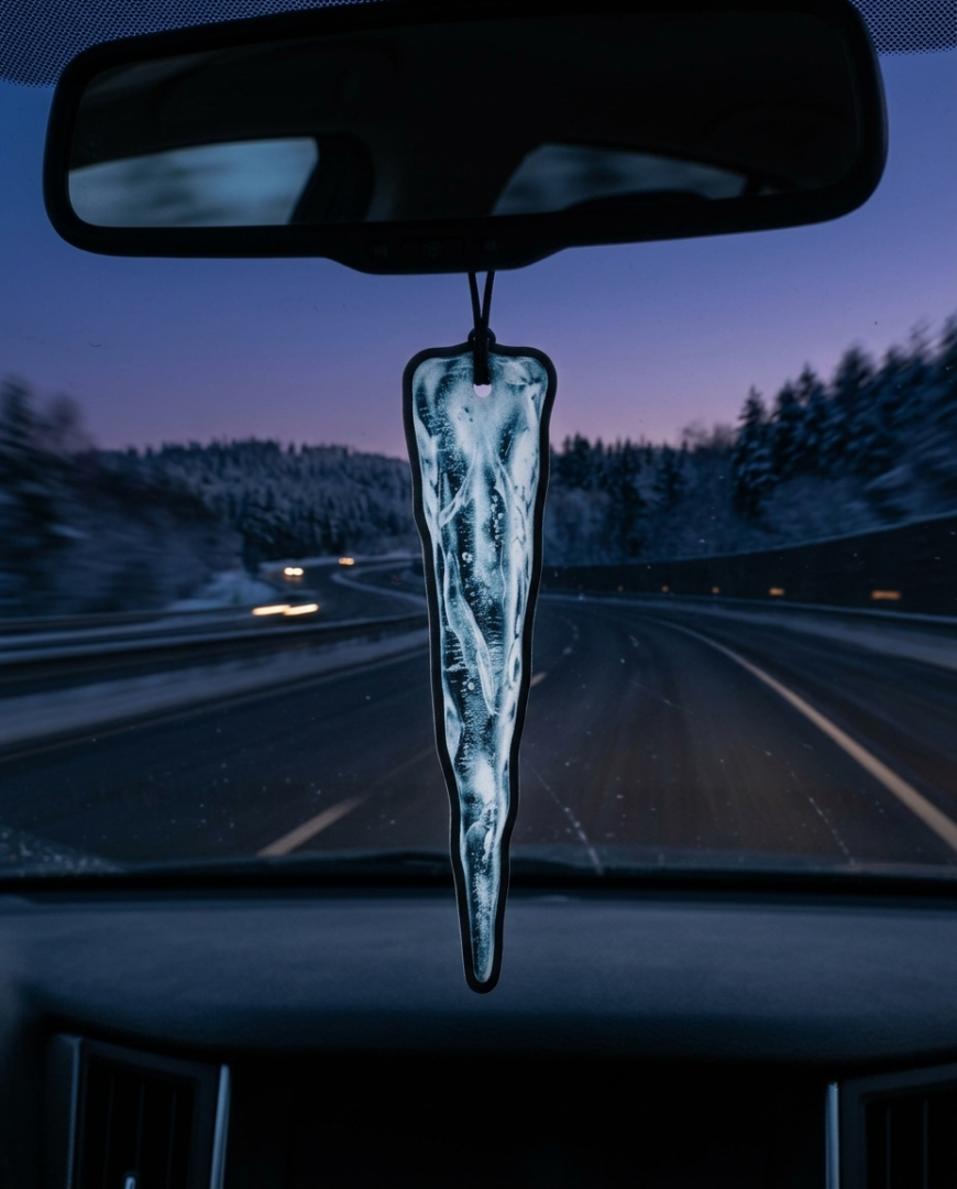 A realistic translucent ice block car air freshener hangs from a rearview mirror inside a moving car, with a blurred winter highway and trees in the background.