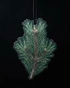 A pine needle-shaped air freshener or car fragrance ornament hanging from a black cord against a solid black background.