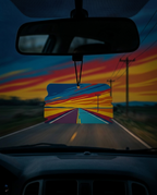 A car air freshener hanging from the rearview mirror, featuring a colorful graphic of a road stretching into the distance under a vibrant sunset sky.