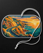A rectangular dog tag with rounded corners, featuring a colorful coastal landscape illustration on a dark background. The tag has a white border and a white hanging rope, photographed against a dark textured backdrop.