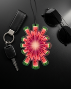 A watermelon-patterned car air freshener or fragrance diffuser hangs from a black cord on a dark surface, styled with a black leather key fob and keys, sunglasses, and a black car key fob on a dark background.