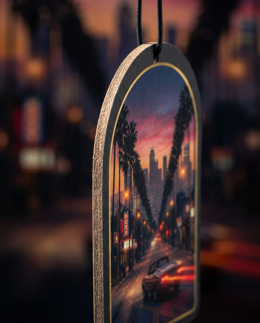 An arched wooden hanging ornament featuring a printed city street scene at dusk with palm trees, glowing streetlights, and a car, suspended by a black cord against a blurred cityscape background.