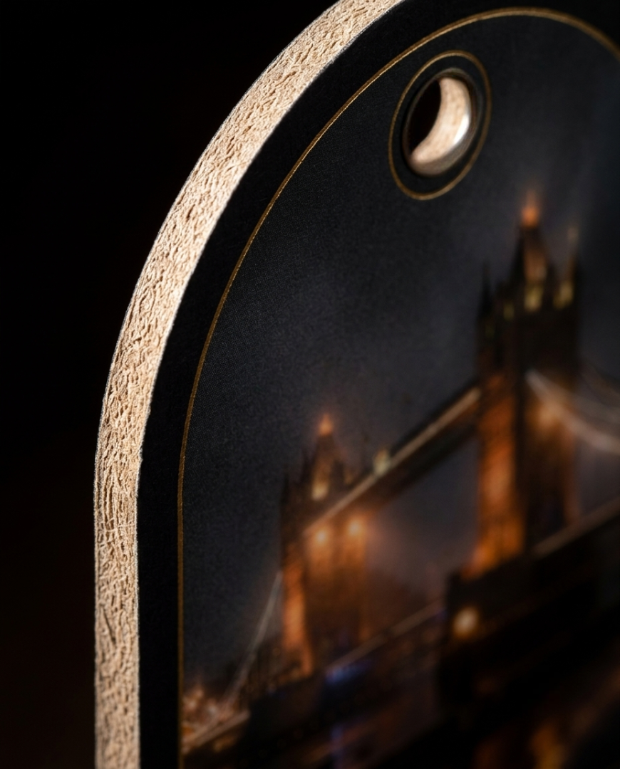 Close-up of a phone case featuring a printed night scene of Tower Bridge with warm golden lights on a dark background, shown against a black backdrop.