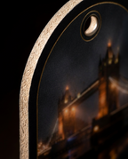 Close-up of a phone case featuring a printed night scene of Tower Bridge with warm golden lights on a dark background, shown against a black backdrop.