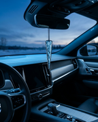 A clear, textured car air freshener hangs from the rearview mirror inside a modern car cabin at dusk.