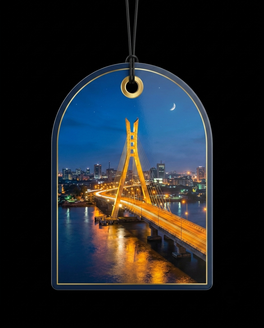 An arched acrylic or glass ornament featuring a printed night photograph of a cable-stayed bridge over water with city lights and a crescent moon, suspended by a black string against a black background.