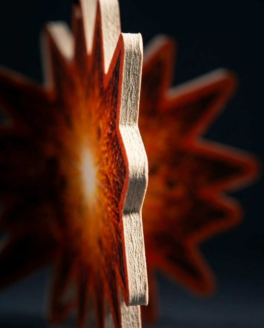 A close-up of a star-shaped wooden ornament or decorative piece with layered wood edges, glowing warmly from within against a dark background.