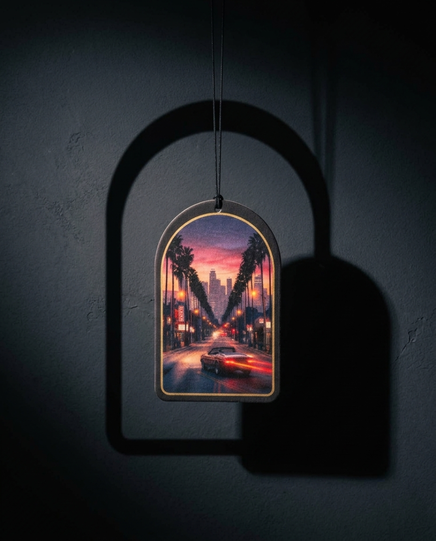 An arched, frame-like wall hanging or ornament with a colorful city street scene at dusk, suspended against a dark wall with a strong shadow cast beside it.