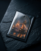 A rectangular glossy ornament or plaque with an arched top and a hanging hole, featuring a printed nighttime city scene with illuminated towers and reflections. It is photographed on a dark textured stone surface.