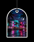 An arched white plastic car air freshener tag with a hanging loop, featuring a colorful printed photograph of a Miami Beach night scene with neon lights, palm trees, and wet streets, shown against a solid black background.