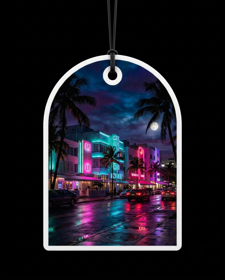 An arched white plastic car air freshener tag with a hanging loop, featuring a colorful printed photograph of a Miami Beach night scene with neon lights, palm trees, and wet streets, shown against a solid black background.