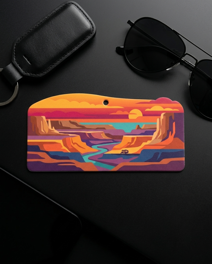 A colorful landscape-themed keychain or card holder with a canyon scene, displayed on a dark surface alongside sunglasses, a black leather key fob, and a phone.