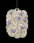 An ornate cream-colored decorative ornament or wall plaque with a scalloped edge, featuring a painted floral and leaf pattern in lavender and gray on a solid black background.
