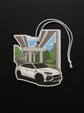 A die-cut car-shaped air freshener or charm featuring a white SUV under an elevated highway overpass, with a white hanging string, shown on a black background.