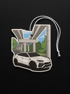 A die-cut car-shaped air freshener or charm featuring a white SUV under an elevated highway overpass, with a white hanging string, shown on a black background.