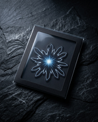 A square black presentation box with a clear lid, featuring a glowing white and blue starburst design on the front, placed on a dark textured stone surface.