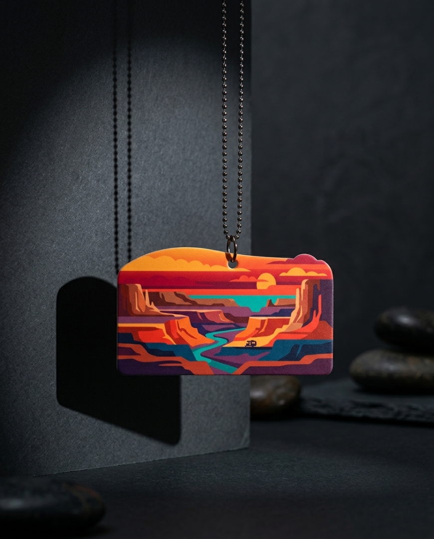 A rectangular pendant necklace featuring a colorful desert canyon landscape illustration, suspended from a dark metal chain against a dark textured background with decorative stones.