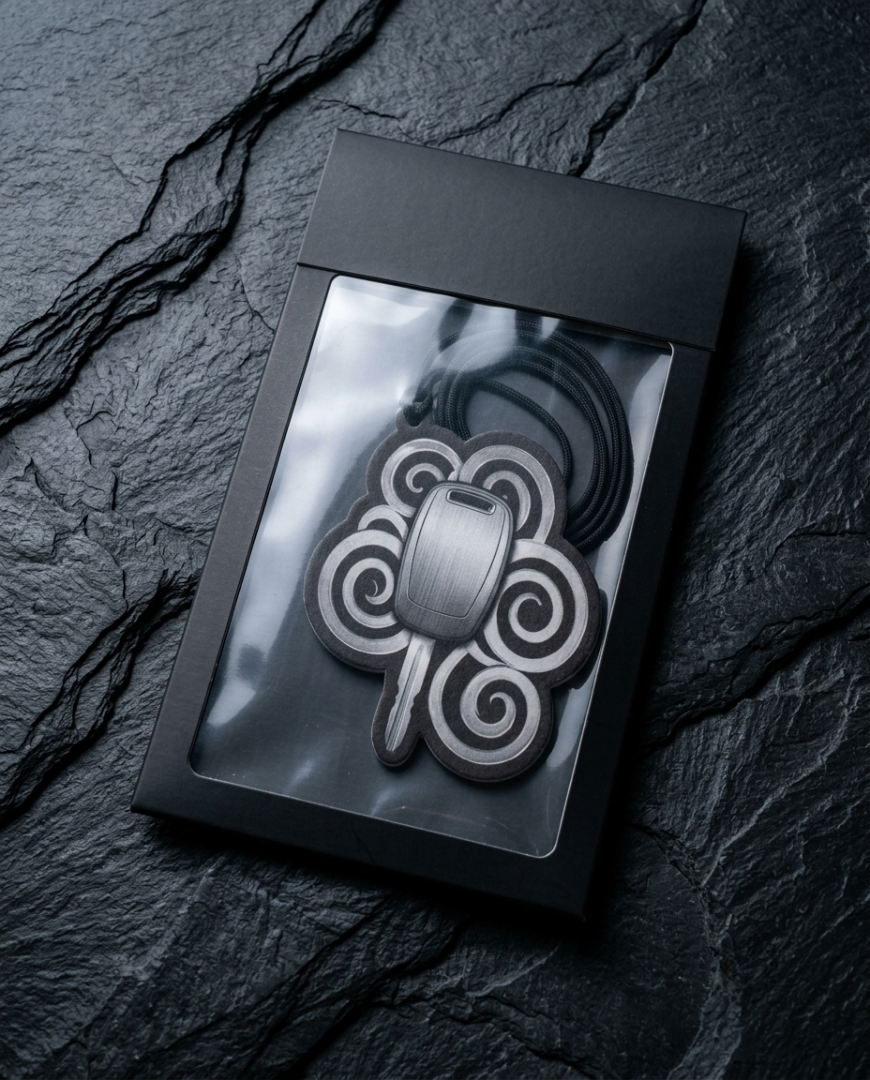 A black metal keychain with a traditional Celtic knot design, presented inside a black gift box with a clear window, set against a dark slate background.
