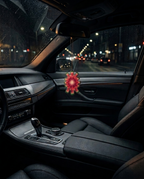 A red and gold flower-shaped car air freshener hangs from the rearview mirror inside a dark car interior at night.