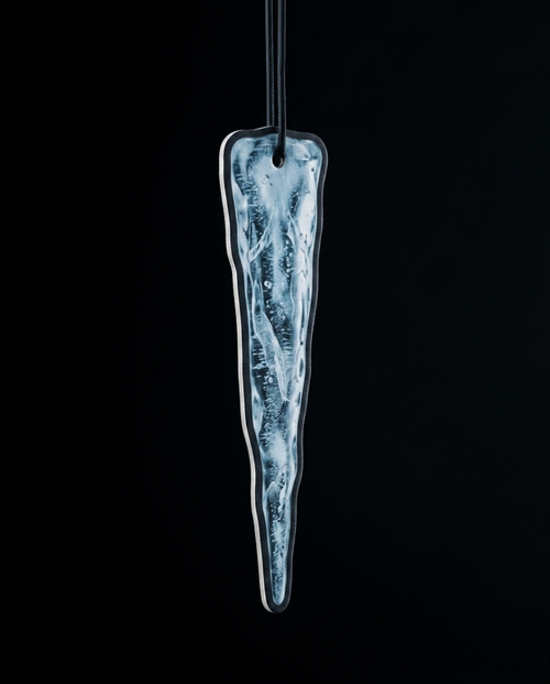 An elongated, tapered glass ornament with a textured, icy blue and white pattern inside a clear glass body, suspended by a black cord against a solid black background.