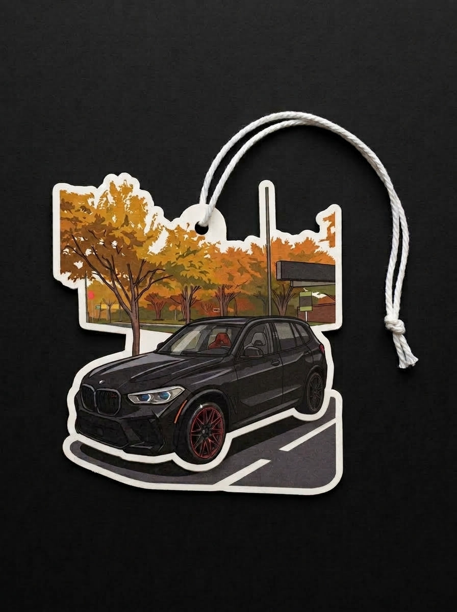 A die-cut car-shaped air freshener or ornament featuring a black BMW SUV in front of an autumn tree scene, with a white hanging cord, shown on a black background.