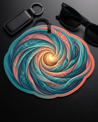 A scalloped circular keychain or bag charm featuring a vibrant swirling abstract pattern in teal, coral, and cream, styled on a dark wooden surface with a black leather key fob and black sunglasses.