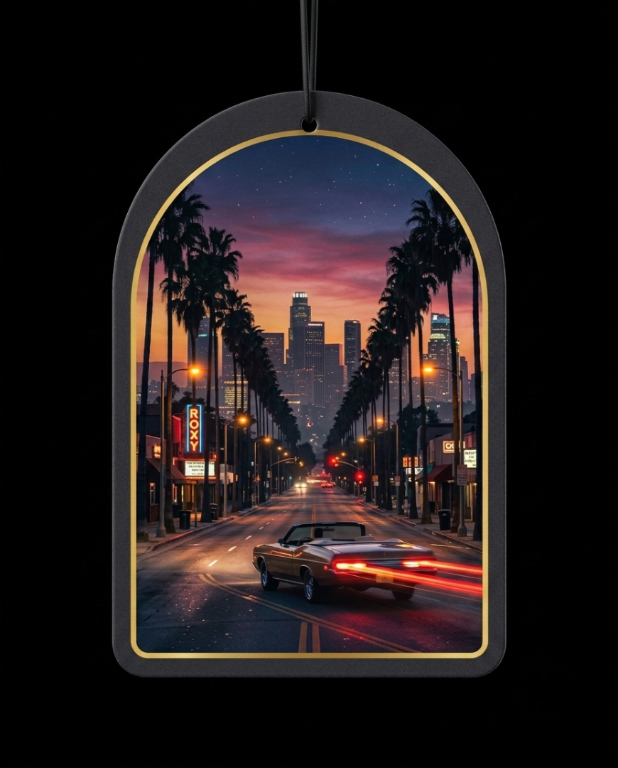 An arched black car air freshener ornament with a gold inner border, featuring a printed sunset cityscape of a palm-lined street with a convertible car and skyscrapers, shown against a black background.