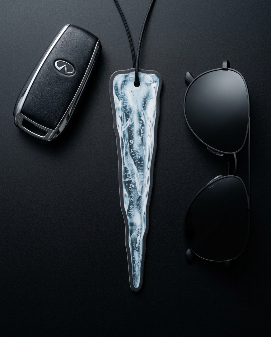 A black car key fob, black sunglasses, and a long sculptural pendant with a white and gray marbled, ice-like pattern, arranged on a dark black background.