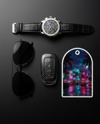 A luxury watch with a black alligator leather strap and silver-toned case, displayed alongside black aviator sunglasses, a carbon-fiber-look car key fob, and an arched metal tag featuring a colorful Miami Beach night scene, all arranged on a dark gray background.
